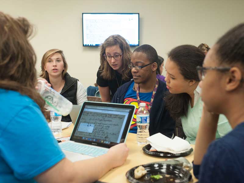 students gathered around a professor's desk collaborating on a project